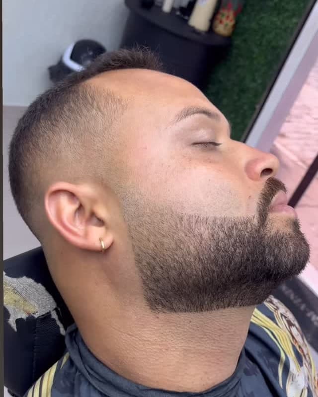 Cliente de olhos fechados, com disfarce e a barba alinhada, visto de perfil